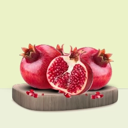 Fresh pomegranates with one cut open to reveal the juicy red seeds displayed on a wooden board.